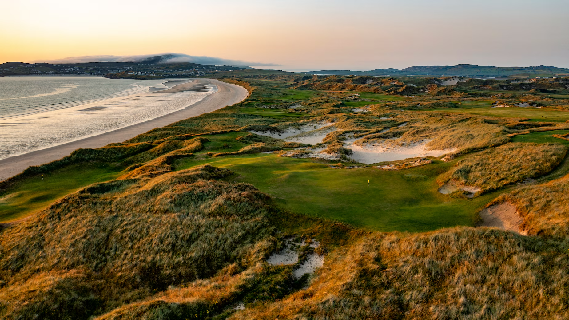 Golf course with sand dunes and a beach at sunset